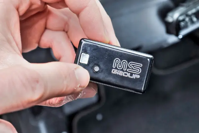 Dispositivo DPF Control sostenido en la mano frente al tablero y la cabina de un vehículo diésel TDI